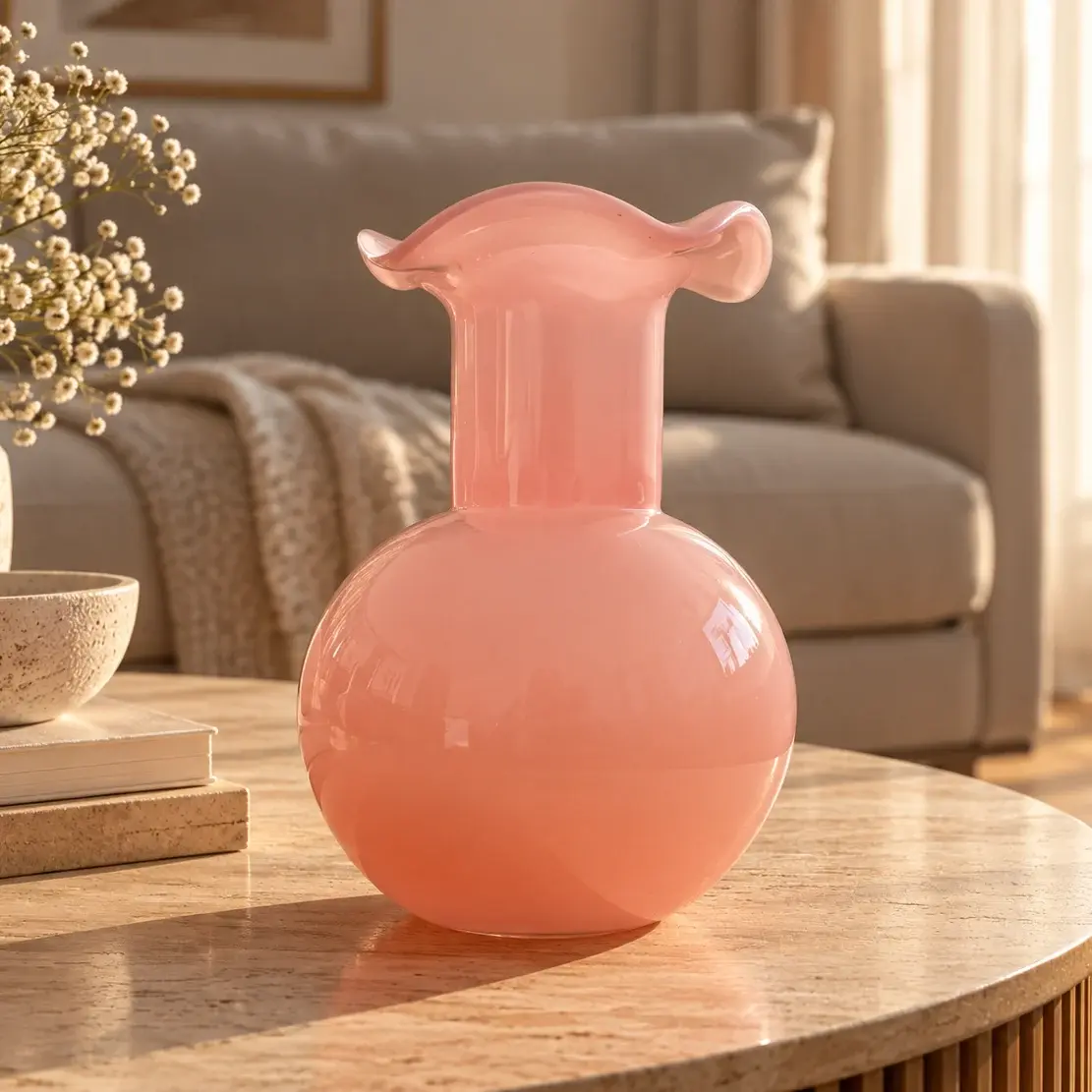 Vase en verre opalin rose poudré, panse sphérique et col évasé aux bords ondulés, posé sur une table en chêne clair